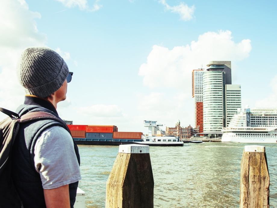 Een toerist kijkt vanaf de kade naar boten op de Maas