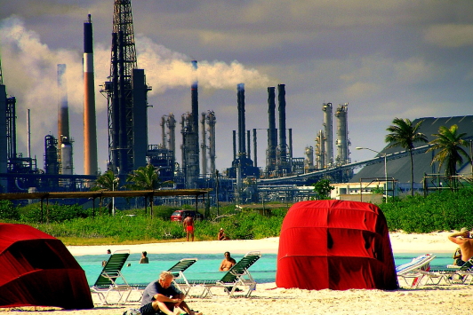 Mensen op een strand op Aruba met op de achtergrond een olierafinaderij