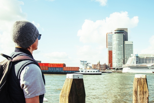 Een toerist kijkt vanaf de kade naar boten op de Maas